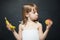 Little girl with apple and banan in the hands. The choice between fruits. Facial expression