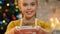 Little girl in apron showing cupcake to camera, proud of homemade pastries