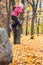 A little girl in an autumn park jumps from a stone covering her face with her hands in a pile of fallen autumn leaves.