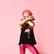 Little girl in backwards cap hiding her face behind crossed hands showing victory signs. Close up shot isolated on pink