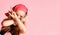 Little girl in backwards cap hiding her face behind crossed hands showing victory signs. Close up shot isolated on pink