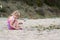 Little girl on the beach plays with sand and a feather