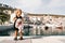 Little girl with a big pink plush hare stands on the pier against the background of the marina with yachts