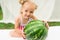 Little girl with a big watermelon on a white mattress in the garden