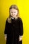 Little girl in a black dress on a yellow background. emotions. anger. angry look