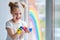 A little girl with blond hair holds paint cans in her hands. The child is engaged in creativity.