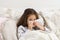 Little girl blow stuffy nose with white handkerchief. Kid in sleepwear lie under blanket. Bed rest, runny nose, snot.