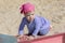 Little girl in a blue dress stands on all fours on the edge of the sandbox, summer sunny day walk