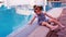 Little girl by the blue pool. A small child is playing by the pool. A beautiful little girl is sitting on the edge of a