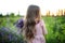 Little girl with bouquet lupins stands with her back facing the sun in floral field. Portrait child with bouquet flowers, view fr