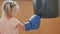 Little girl in boxing gloves is beating by the punching bag
