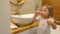 A little girl brushes her teeth in the bathroom and gives a thumbs up