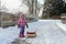 The little girl is carrying sled in winter snow forest