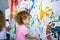 A little girl of Caucasian appearance draws with a long brush on a multi-colored wall with coloring.