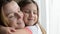 Little girl child, daughter hugs and kisses mother near the window, happy family