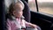 Little girl in a child seat looks out the window while driving a car