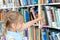 Little girl chooses, takes book with fairy tales from shelf in children`s library.Special reading kids room.Many shelves with