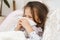 Little girl with closed eyes blow stuffy nose with handkerchief. Kid in sleepwear lie under blanket and have bed rest.