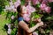 Little girl with closed eyes enjoying her leisure time in garden, hugging blooming tree branch pink flowers