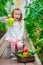 Little girl collecting crop cucumbers and tomatos in greenhouse. Portrait of kid with big sweet green peper in hands