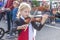 Little girl concentrating on playing violin at farmers market as little boy with parents looks at her