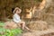 Little girl in country style clothes sitting on haystack in hayloft