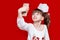 Little girl with crazy face hold telephone and take picture on red background