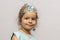 A little girl in a crown and earrings demonstrates toy rings on her fingers, children`s jewelry and costume jewelry.