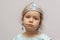 A little girl in a crown and earrings demonstrates toy rings on her fingers, children`s jewelry and costume jewelry.