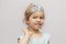 A little girl in a crown and earrings demonstrates toy rings on her fingers, children`s jewelry and costume jewelry.