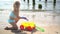 Little girl with curly blond hair playing with sand ant toy cart on sea shore