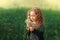 A little girl with curly hair blows on white dandelions in the summer in the park. Portrait of a large