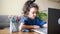 Little girl with curly hair uses a laptop to do schoolwork at home and write notes. online lesson at home