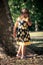 Little girl in cute summer dress walk in park by huge tree