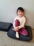 Little girl with dark hair smiles, sits on the floor. Optimistic portrait.