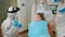 Little girl with dental bib and ppe suit listening pediatric dentist in coverall