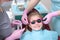 A little girl at a dentist appointment. The child is put on bright safety glasses. Photo inside the clinic