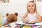 Little girl drawing with her toy bear keeping company