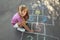 Little girl drawing hopscotch with chalk on asphalt outdoors. Happy childhood