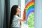 Little girl drawing rainbow on window. Stay at home concept