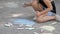 A little girl draws chalk on the asphalt. The child draws the sun in the park.