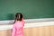 Little girl draws with chalk on a blackboard. View from the back. The child performs a learning task. Babe starts school in first