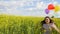 Little girl in a dress running through yellow wheat field with balloons in hand