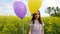 Little girl in a dress running through yellow wheat field with balloons in hand. slow motions