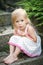 A little girl in a dress sits on the stone steps in the garden. Bare feet, smile