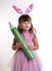 Little girl dressed as the Easter bunny standing on white background and holding pencil