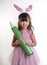 Little girl dressed as the Easter bunny standing on white background and holding pencil