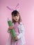 Little girl dressed as the Easter bunny standing on white background and holding pencil. Child Easter Holiday Concept.