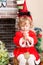 Little girl dressed costume Santa Claus by fireplace. Christmas