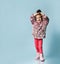 Little girl dressed in pink faux fur coat, pants and boots. She smiling, gesticulating, posing on blue background. Full length